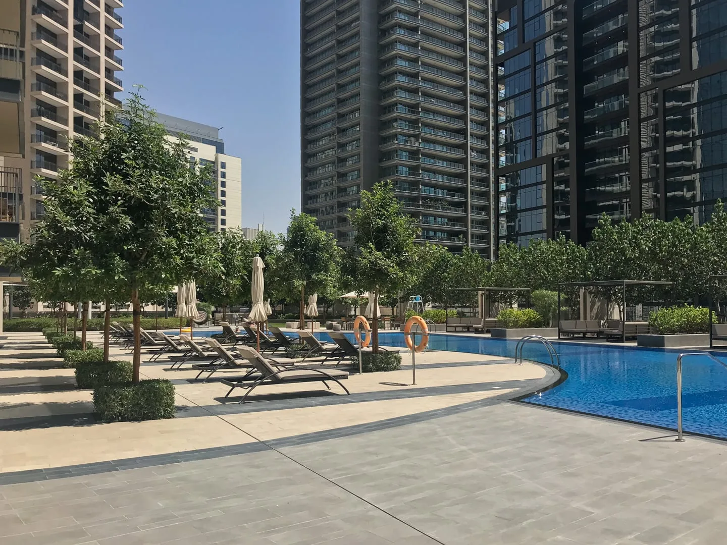 Una zona de piscina al aire libre con asientos, árboles y edificios altos.