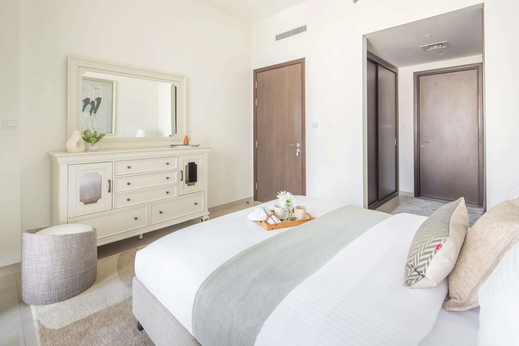 Un dormitorio luminoso con una cama tendida, una cómoda y una puerta.
