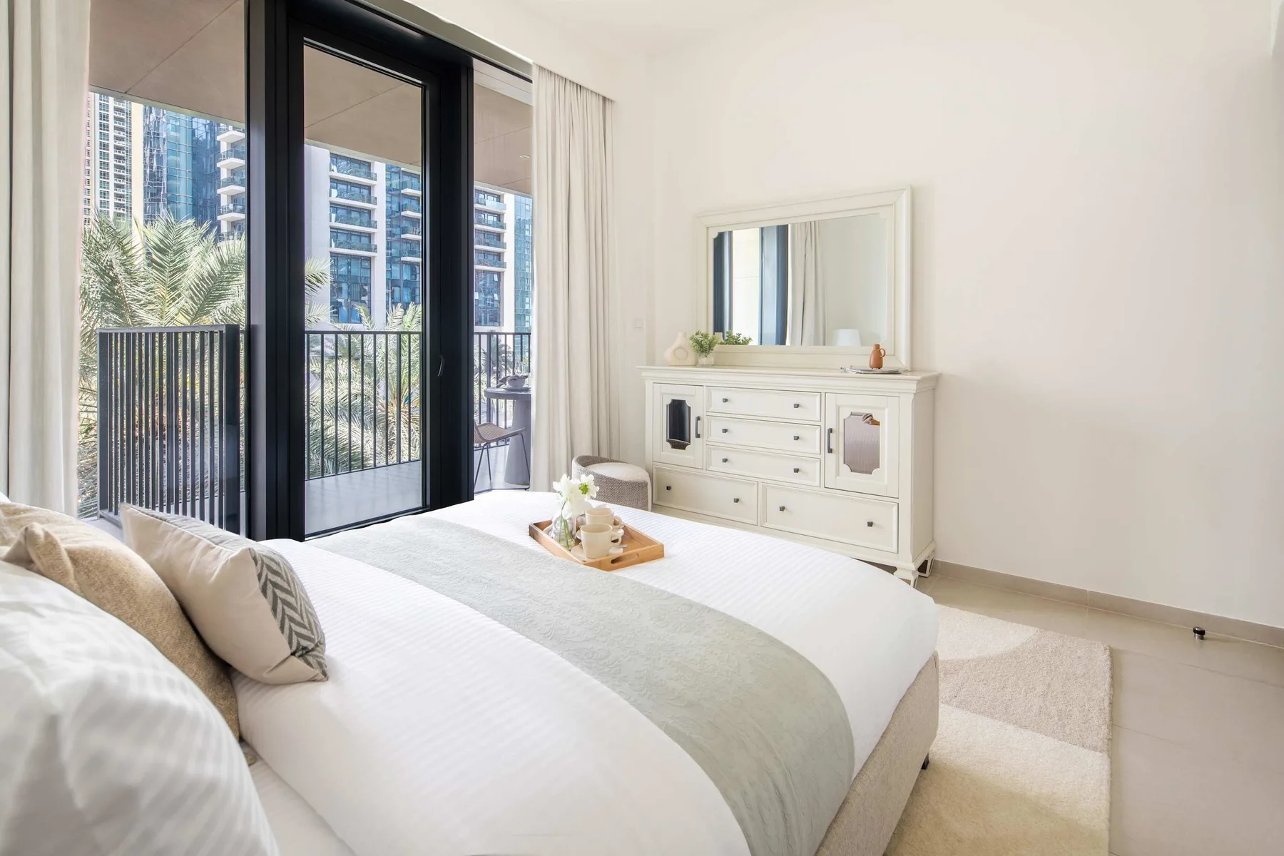 Un dormitorio luminoso con una cama junto a grandes ventanales y una cómoda.
