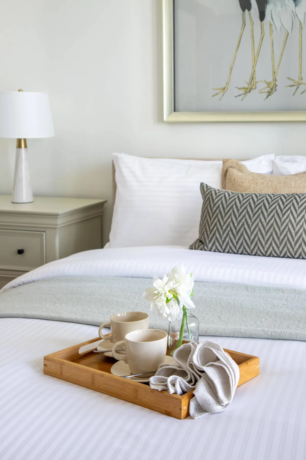 Un dormitorio ordenado con una bandeja de desayuno y flores sobre la cama.