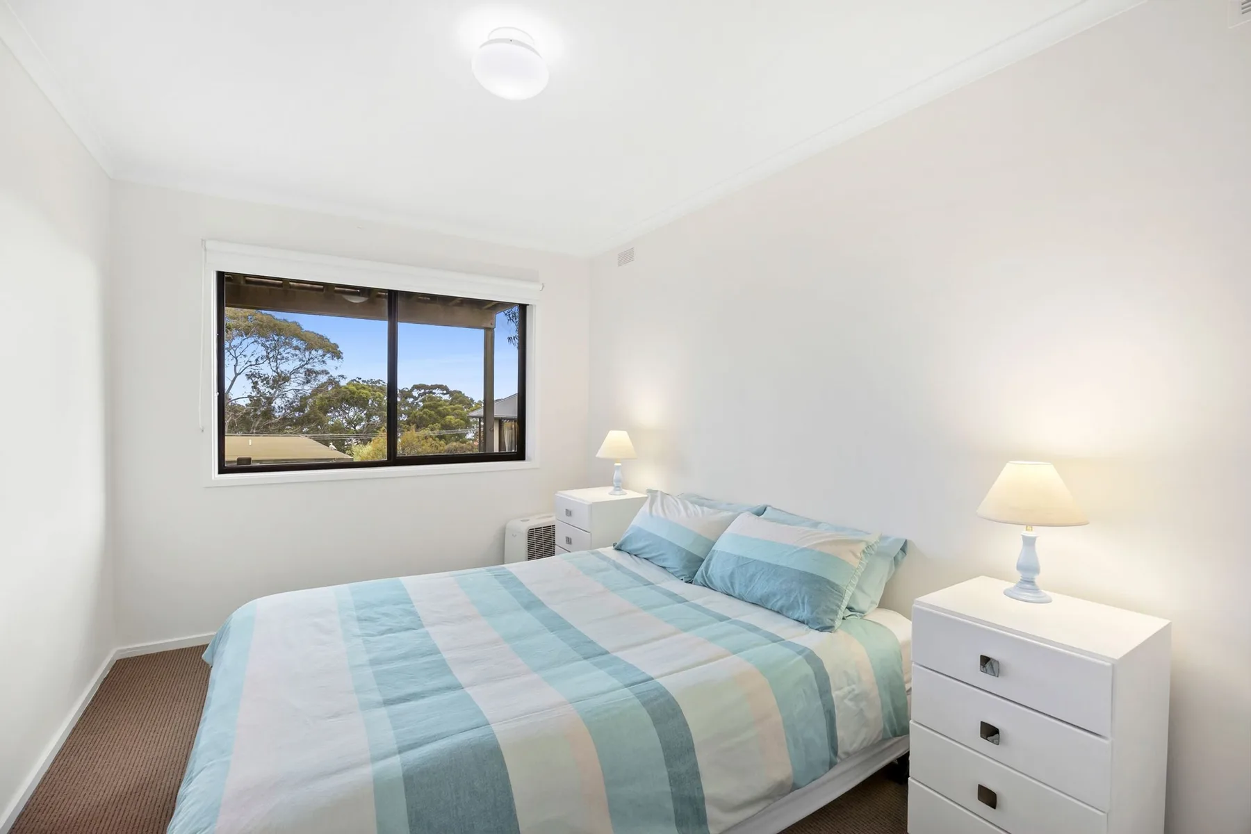 Un dormitorio luminoso con una cama y una ventana con vistas a los árboles.