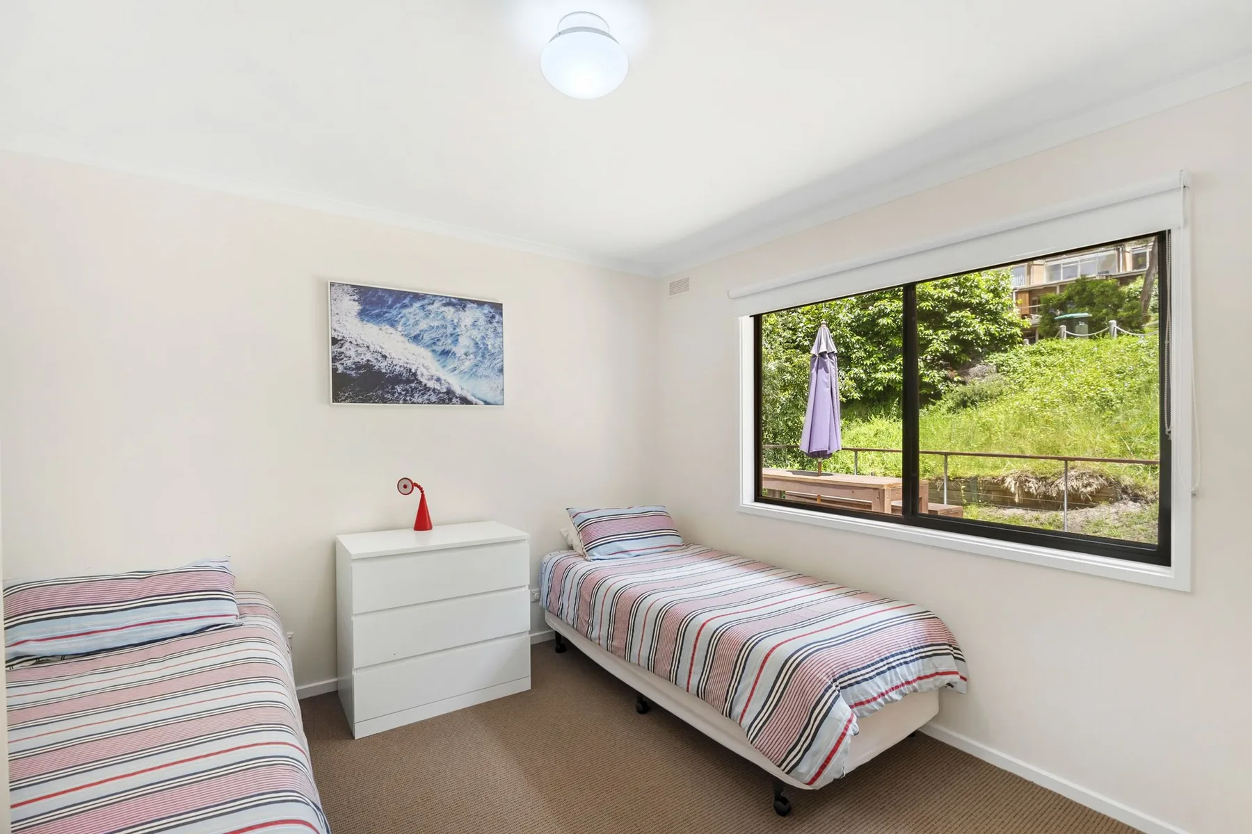 Un dormitorio luminoso con ropa de cama a rayas y una ventana amplia con vistas al jardín.