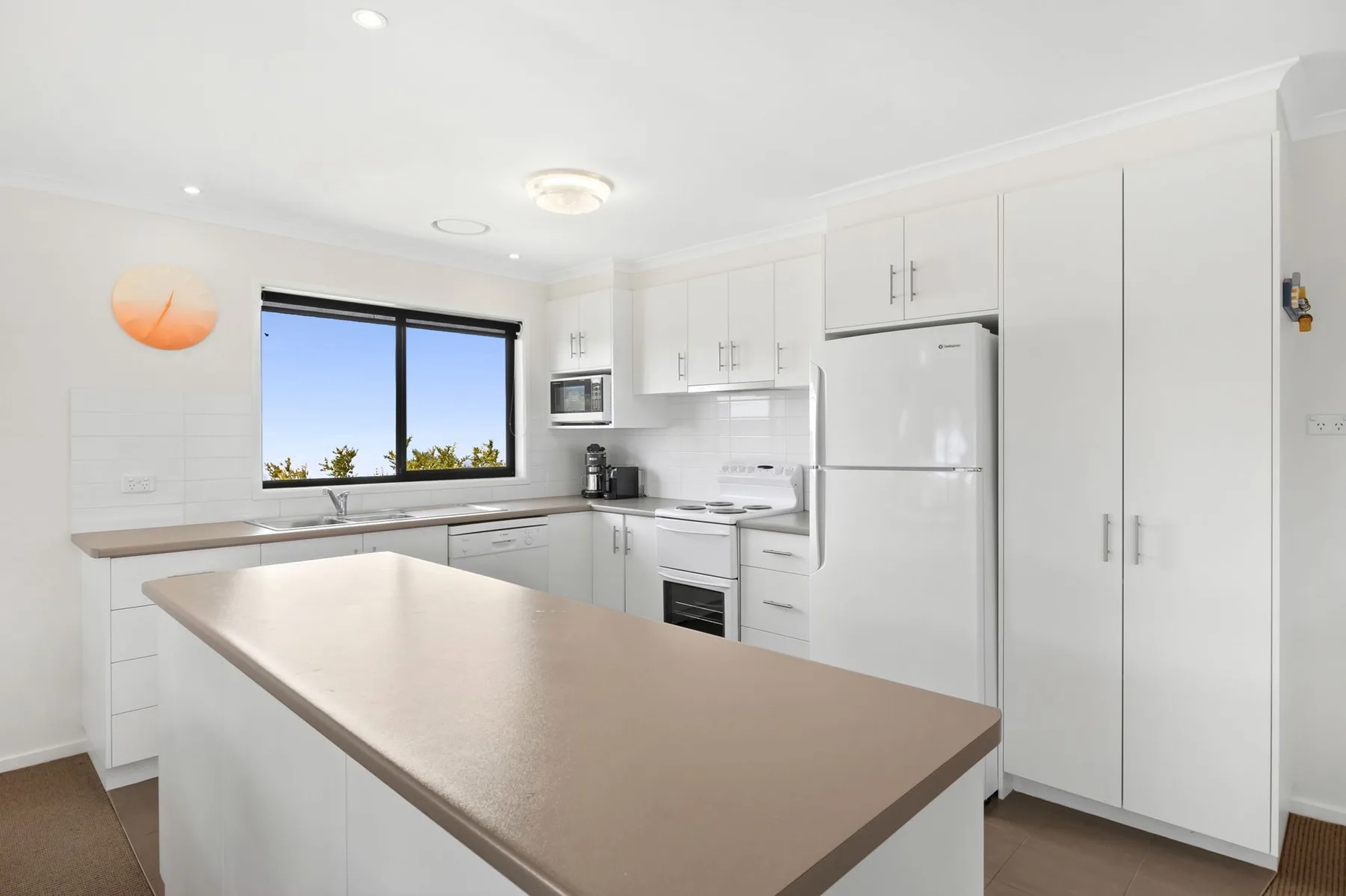 Una cocina luminosa con gabinetes blancos, un refrigerador y una isla grande.