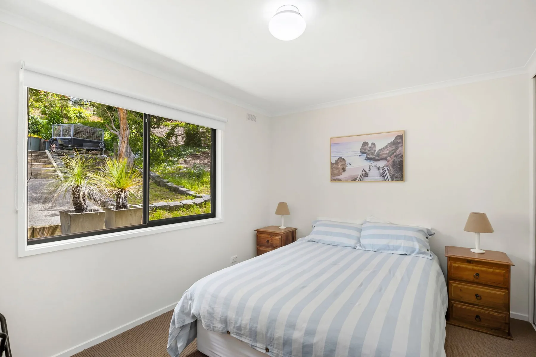 Dormitorio con una cama junto a una ventana amplia con vistas a la vegetación.