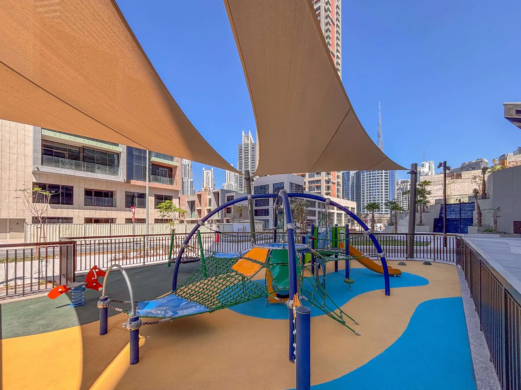 Un parque infantil al aire libre con estructuras para trepar está bajo grandes toldos.