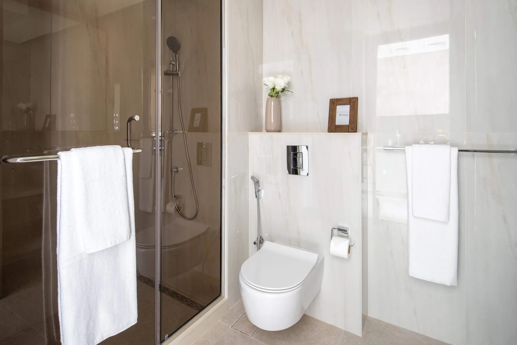 Un baño moderno con ducha de cristal, inodoro y toallas blancas.