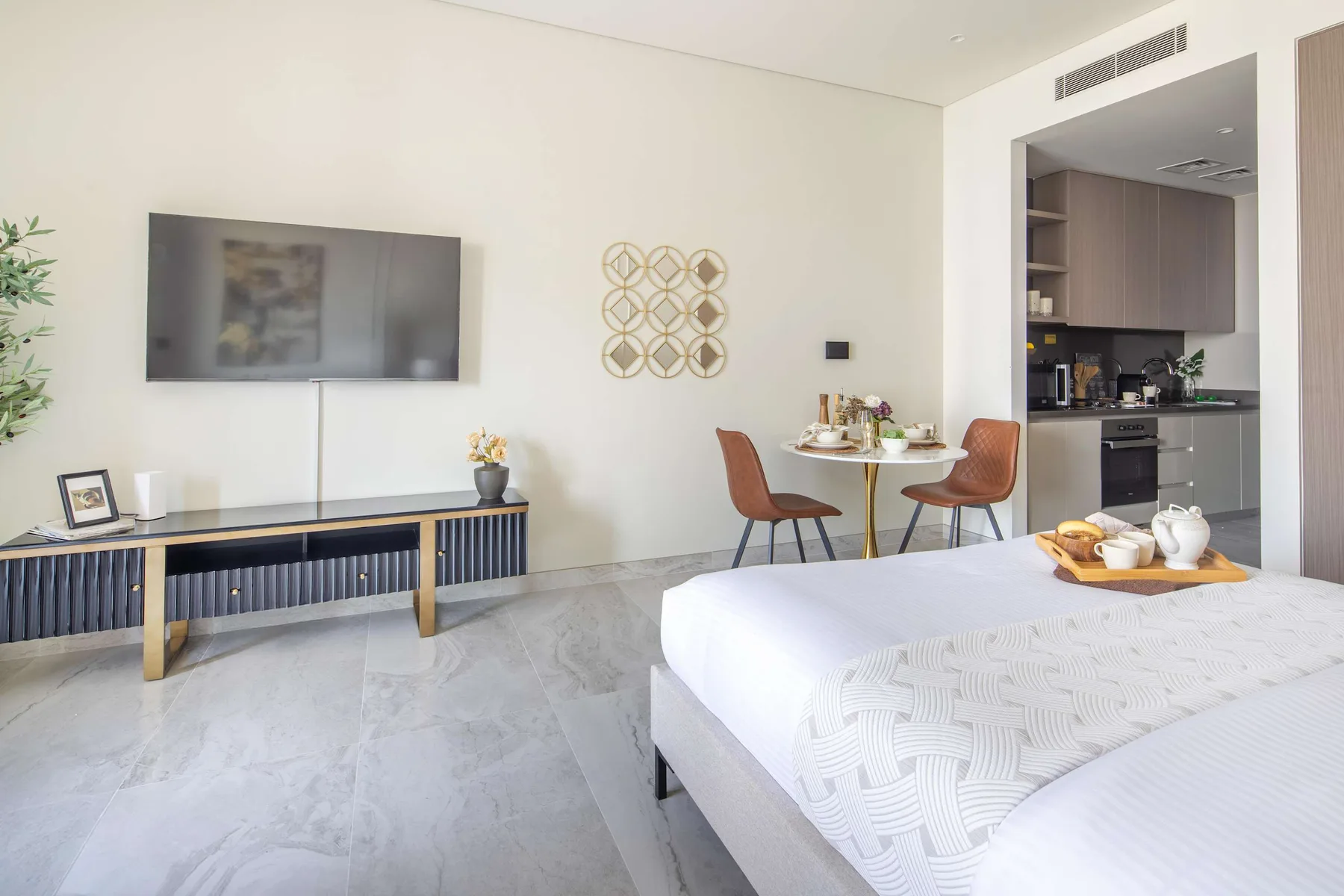 Un dormitorio luminoso con cama, televisor y una pequeña mesa de comedor junto a la cocina.