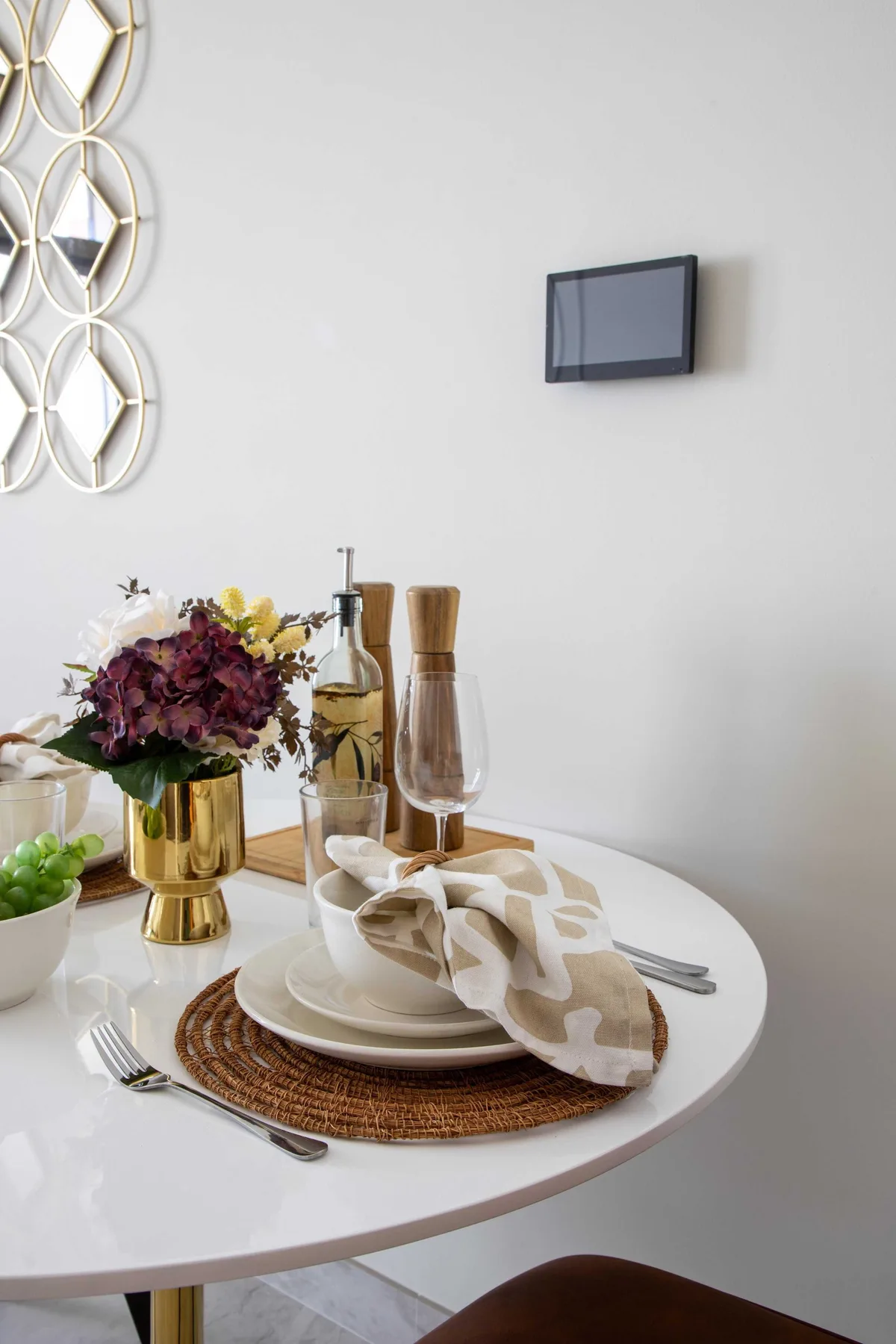 Una mesa de comedor está puesta con platos, una servilleta doblada y un arreglo floral.