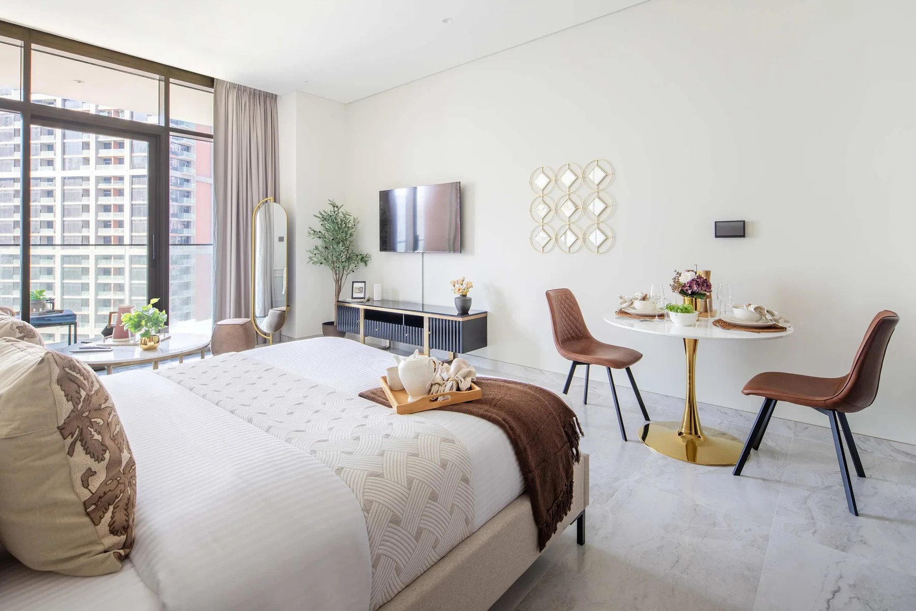 Un dormitorio luminoso con una cama, una zona de estar y grandes ventanas.