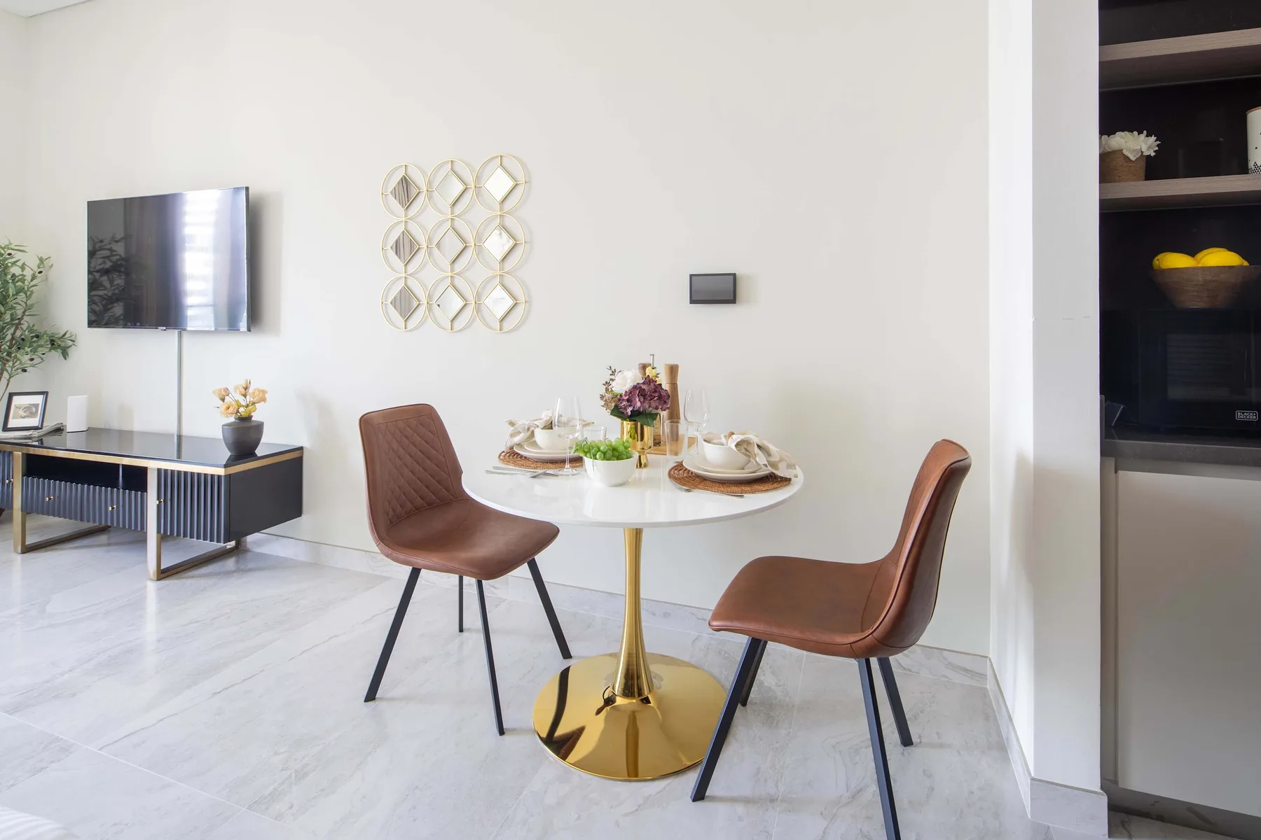 Un comedor con una mesa redonda, asientos marrones y un televisor en la pared.