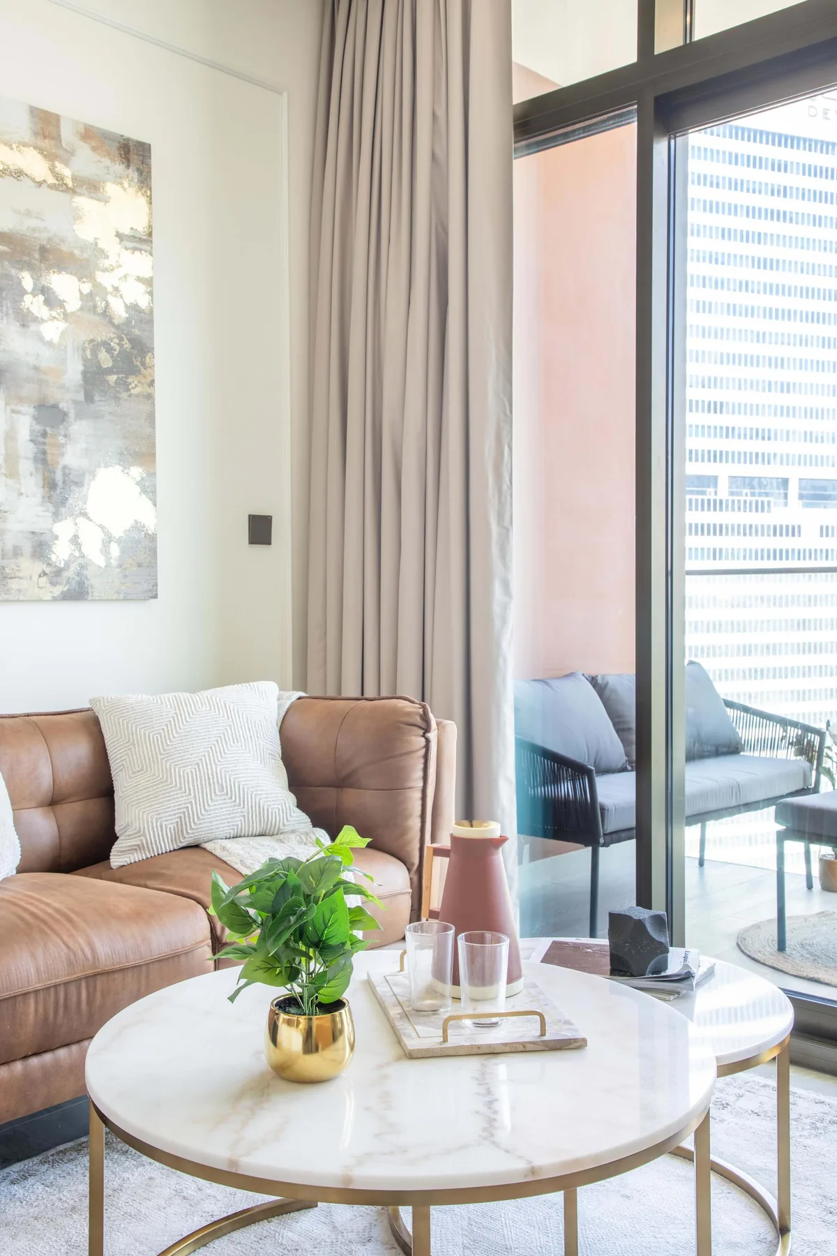 Una sala luminosa con sofá marrón, mesa de centro redonda y ventanales de piso a techo.