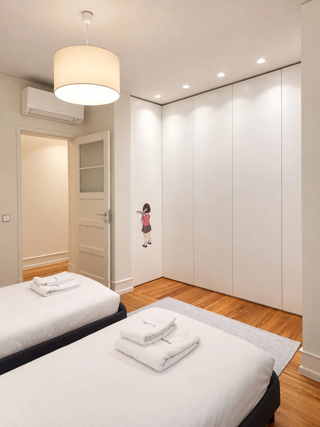 Un dormitorio luminoso con dos camas, ropa de cama blanca y armarios empotrados.