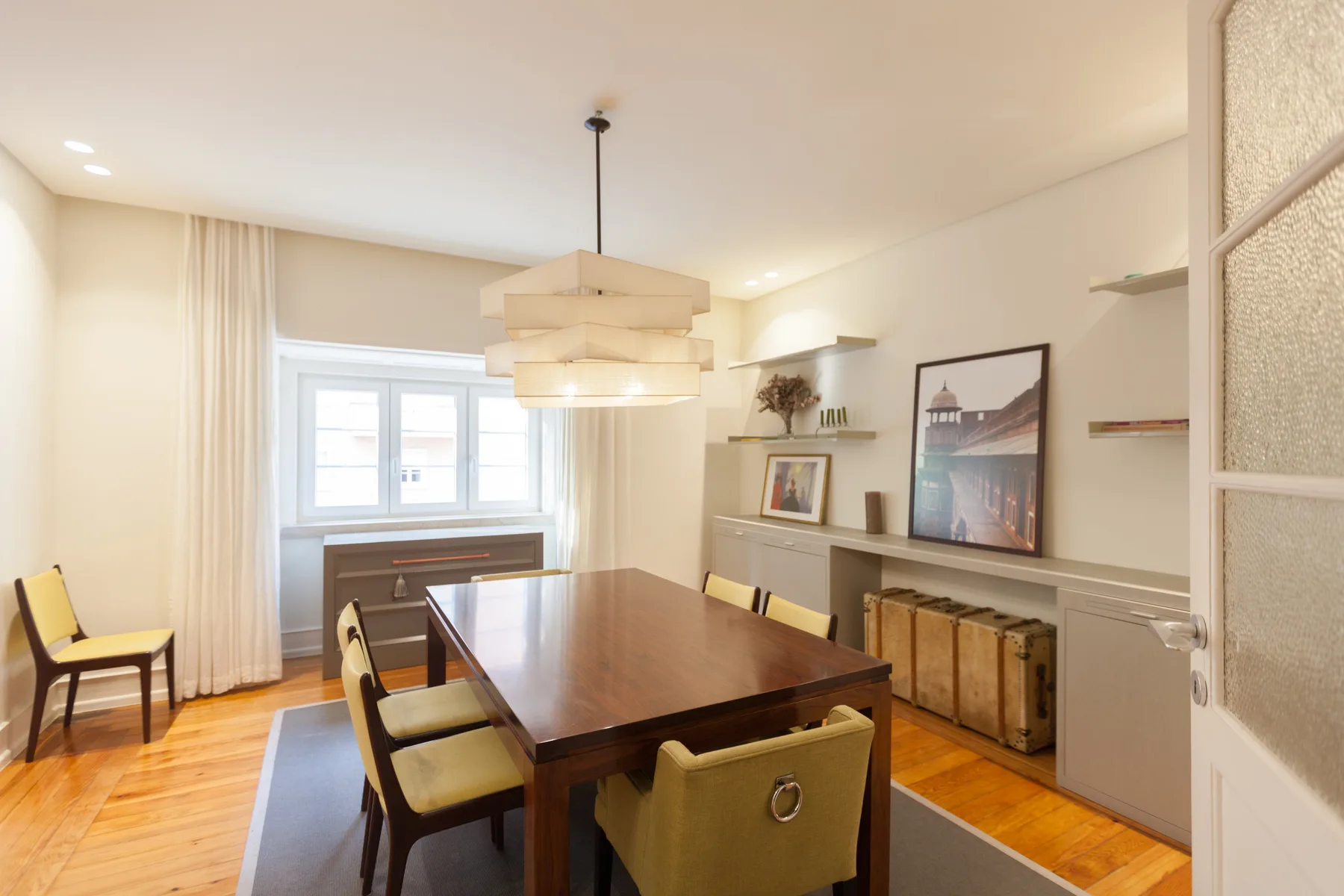 Un comedor con una mesa larga de madera y sillas bajo lámparas colgantes.