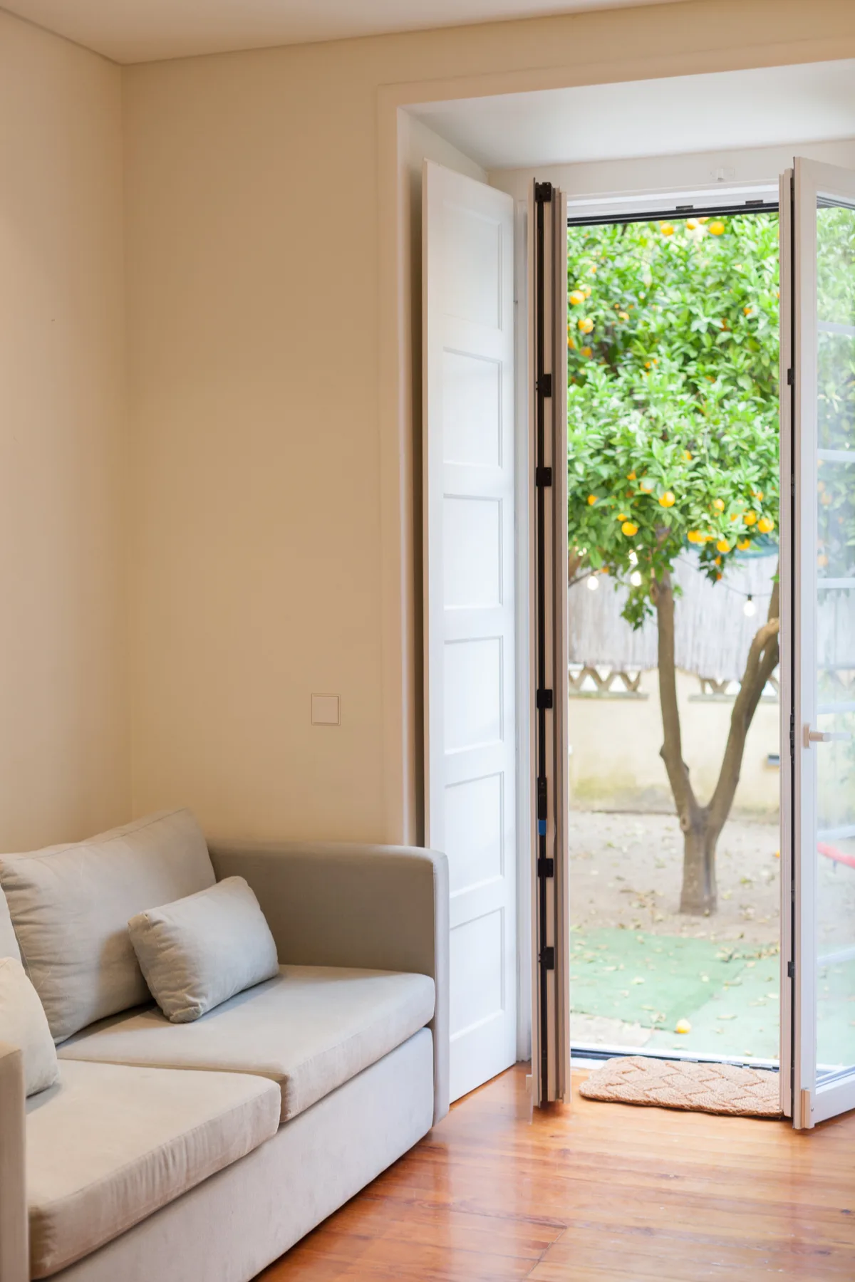 Una sala luminosa con asientos claros y una puerta abierta a un jardín frondoso.