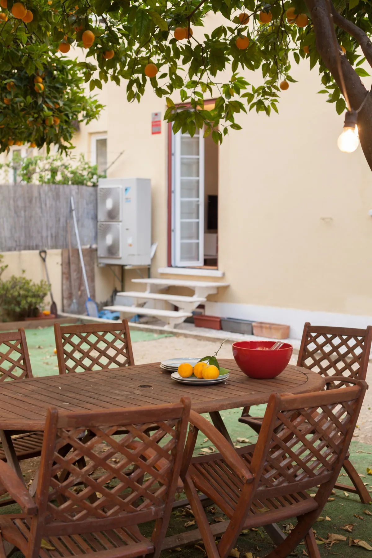 Un patio ajardinado con una mesa de comedor al aire libre bajo un árbol frutal.