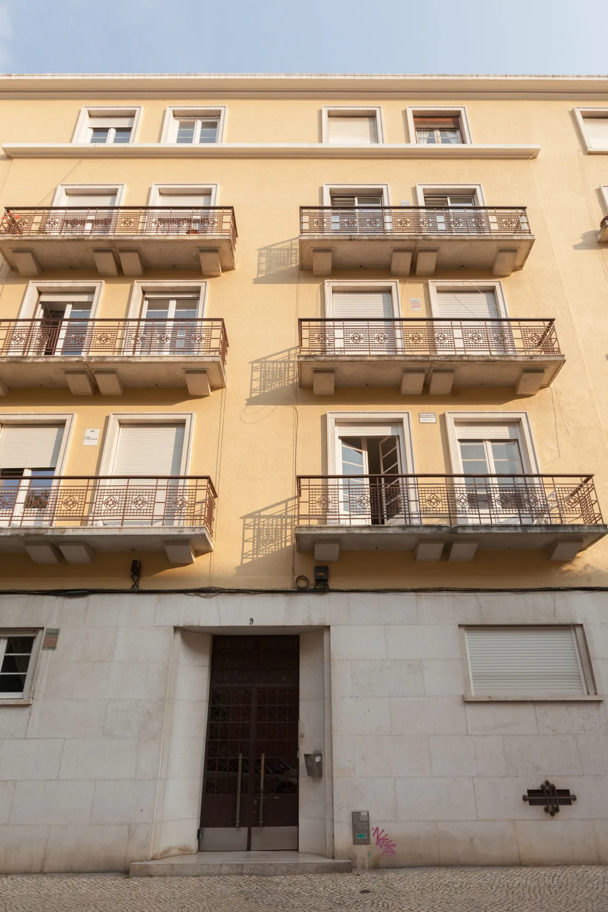 Fachada de un edificio de apartamentos claro con filas de balcones y ventanas.