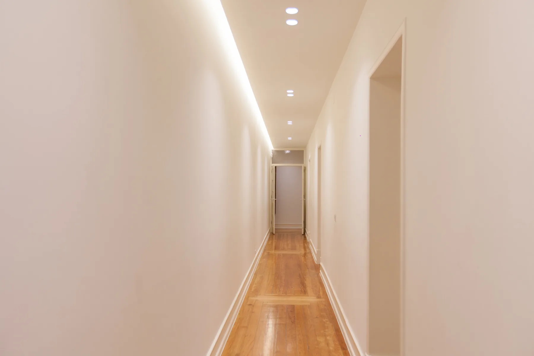Un pasillo luminoso con suelo de madera y luces empotradas en el techo.