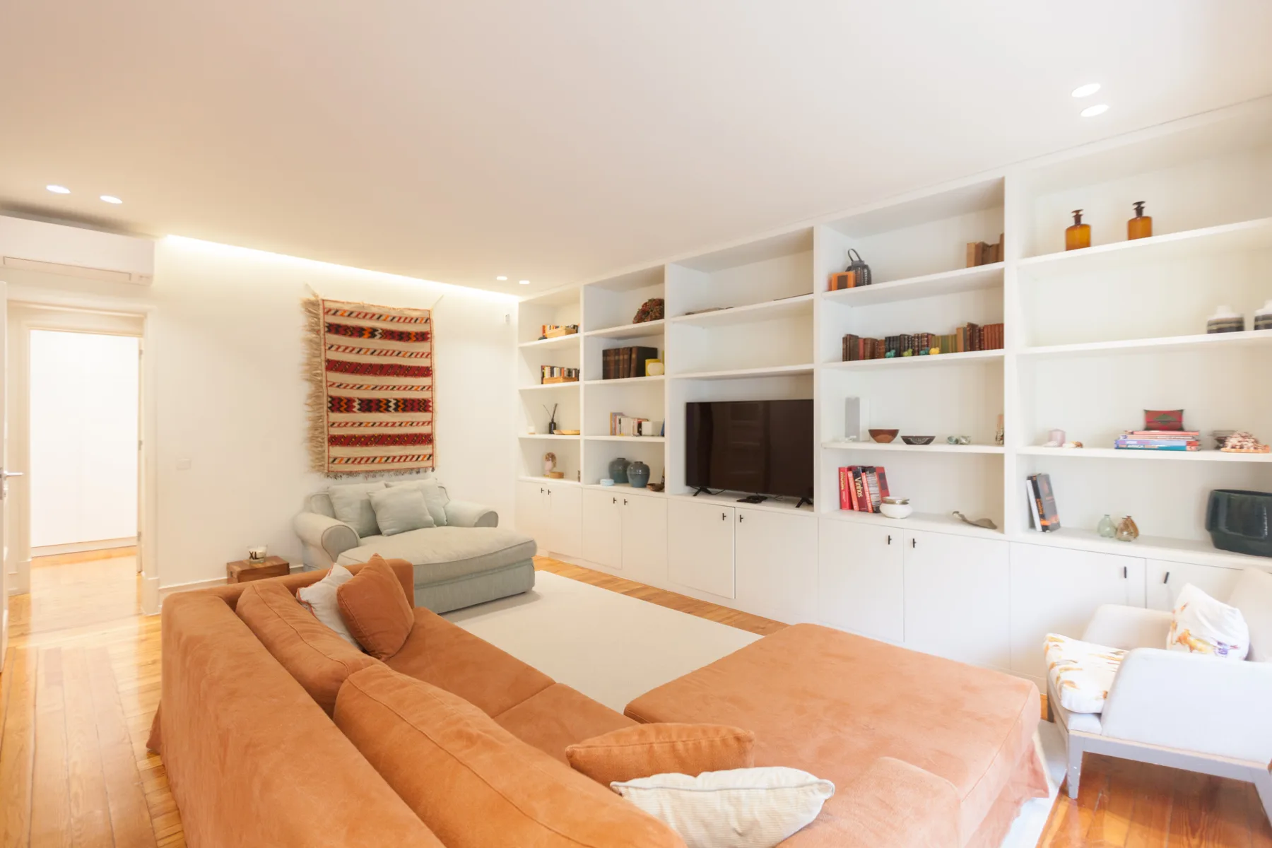 Una sala luminosa con asientos, estanterías blancas empotradas y un televisor.
