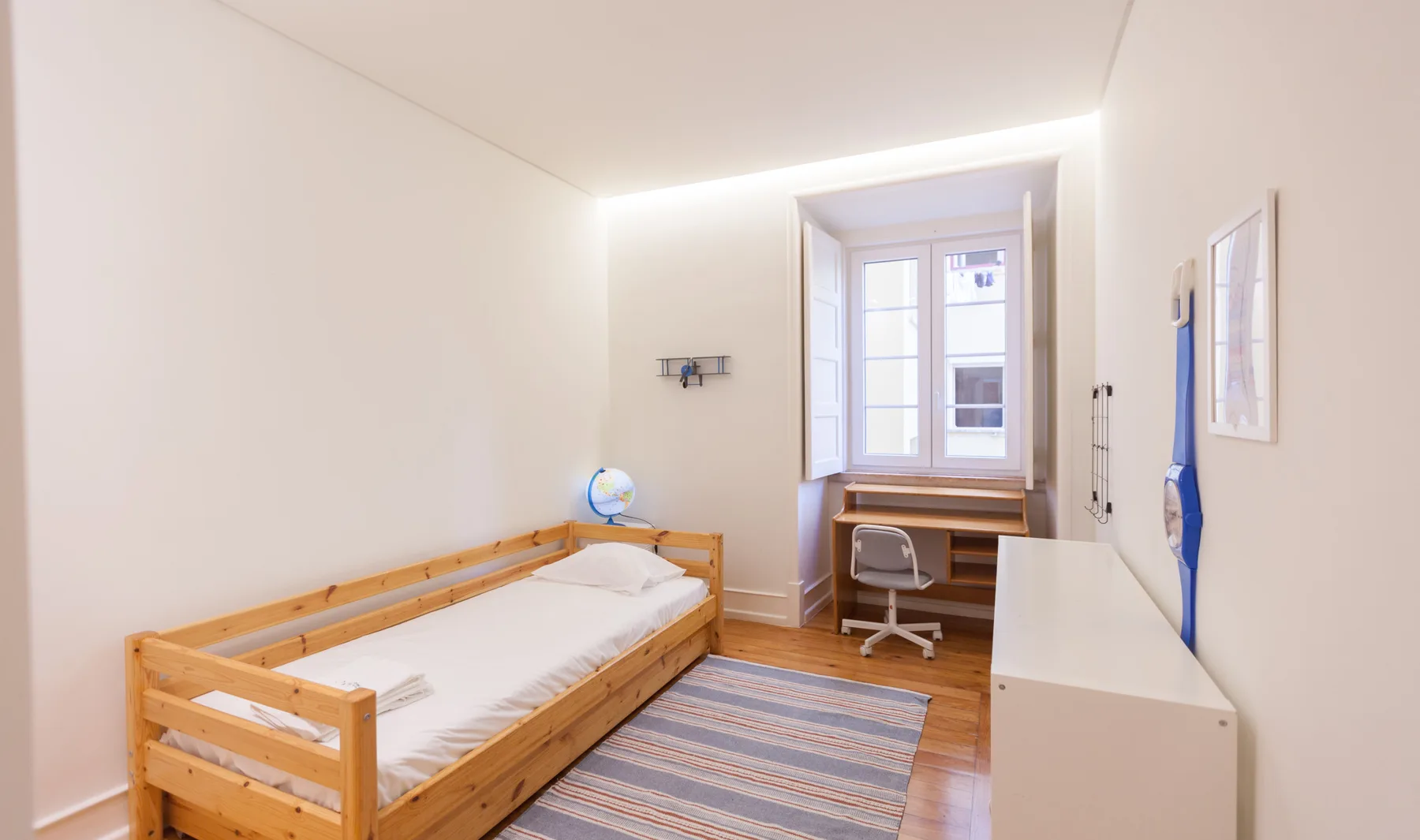 Un dormitorio luminoso con cama de madera, escritorio y ventana.