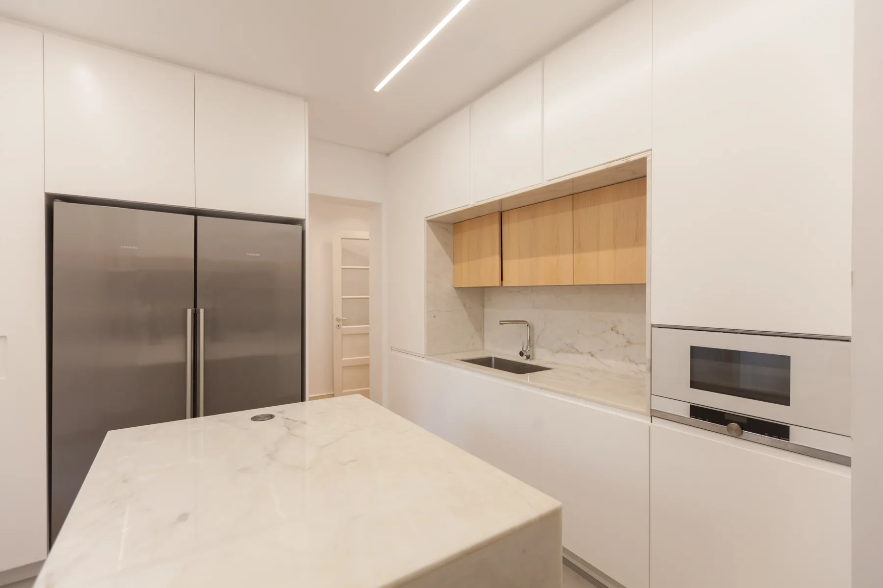 Una cocina moderna con gabinetes blancos, una isla de piedra y electrodomésticos de acero inoxidable.