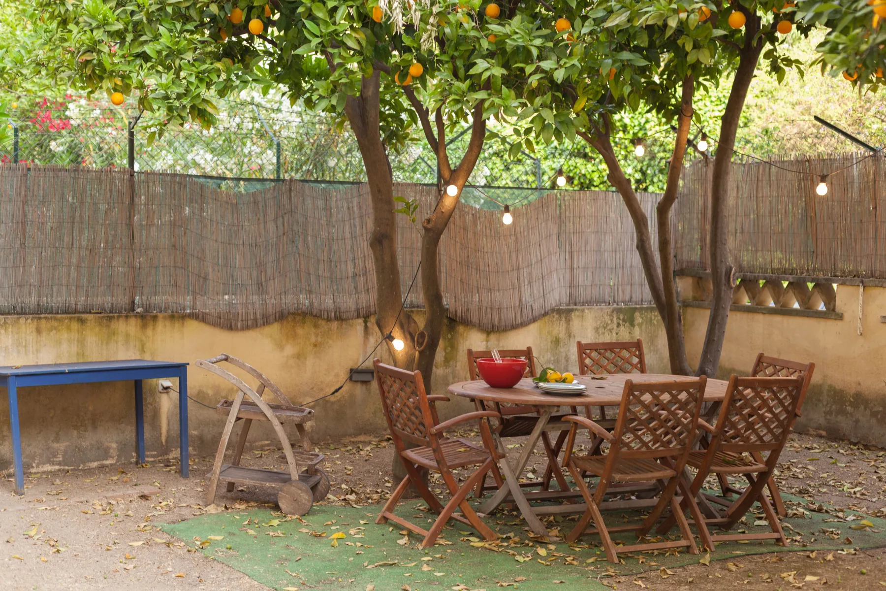 Un patio ajardinado con una mesa de comedor de madera bajo árboles frondosos.