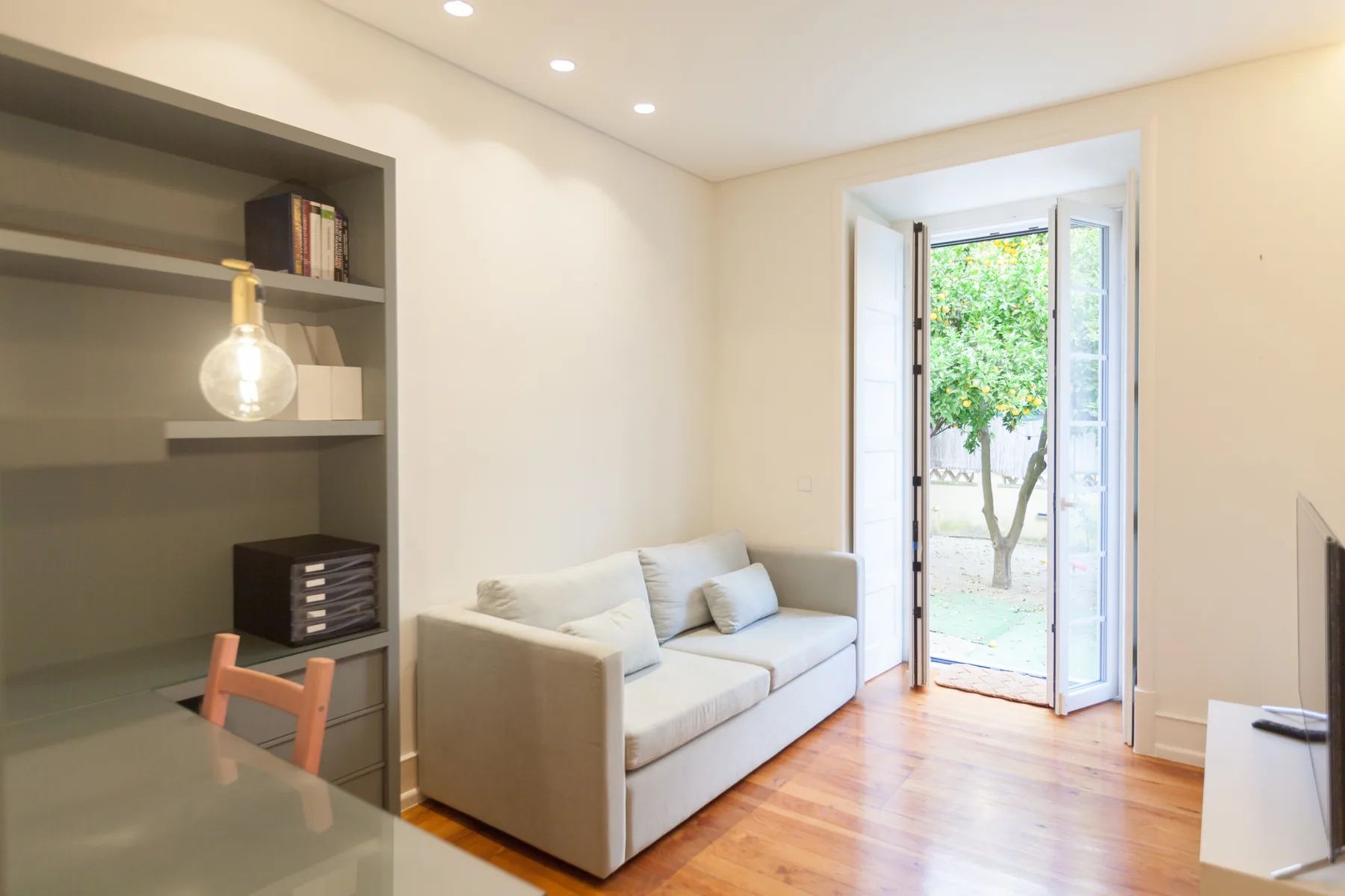 Una sala luminosa con un sofá claro junto a puertas de vidrio abiertas.