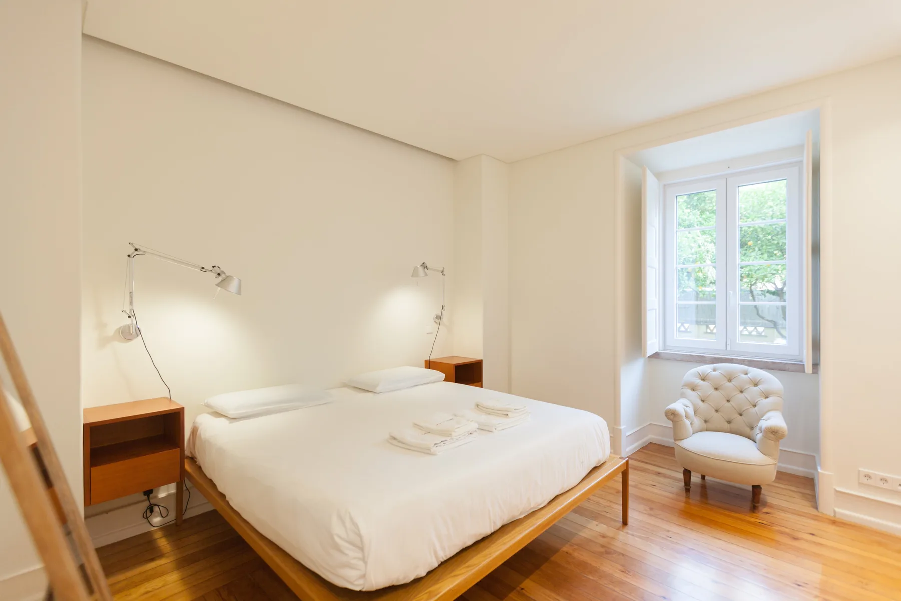Un dormitorio luminoso con una cama y un sillón junto a la ventana.