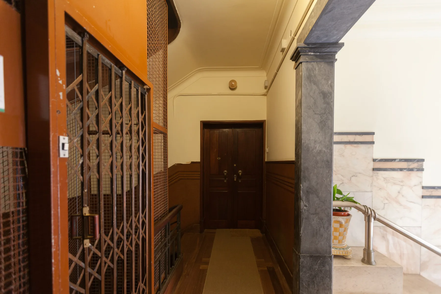 Entrada de un edificio de apartamentos con una reja metálica y un pasillo que conduce a una puerta de madera.