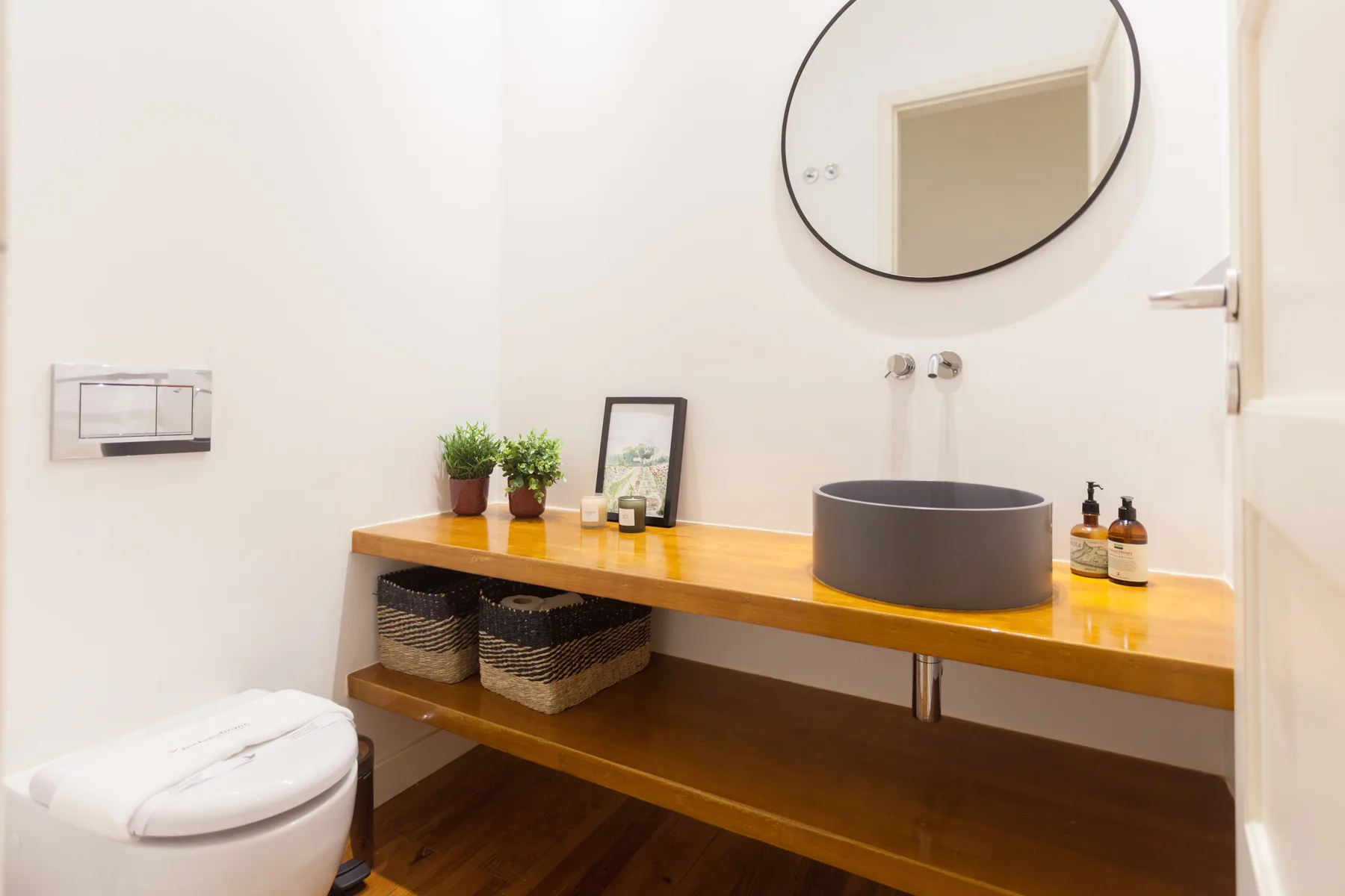 Un lavabo de baño tiene una encimera de madera, un recipiente redondo y un espejo.