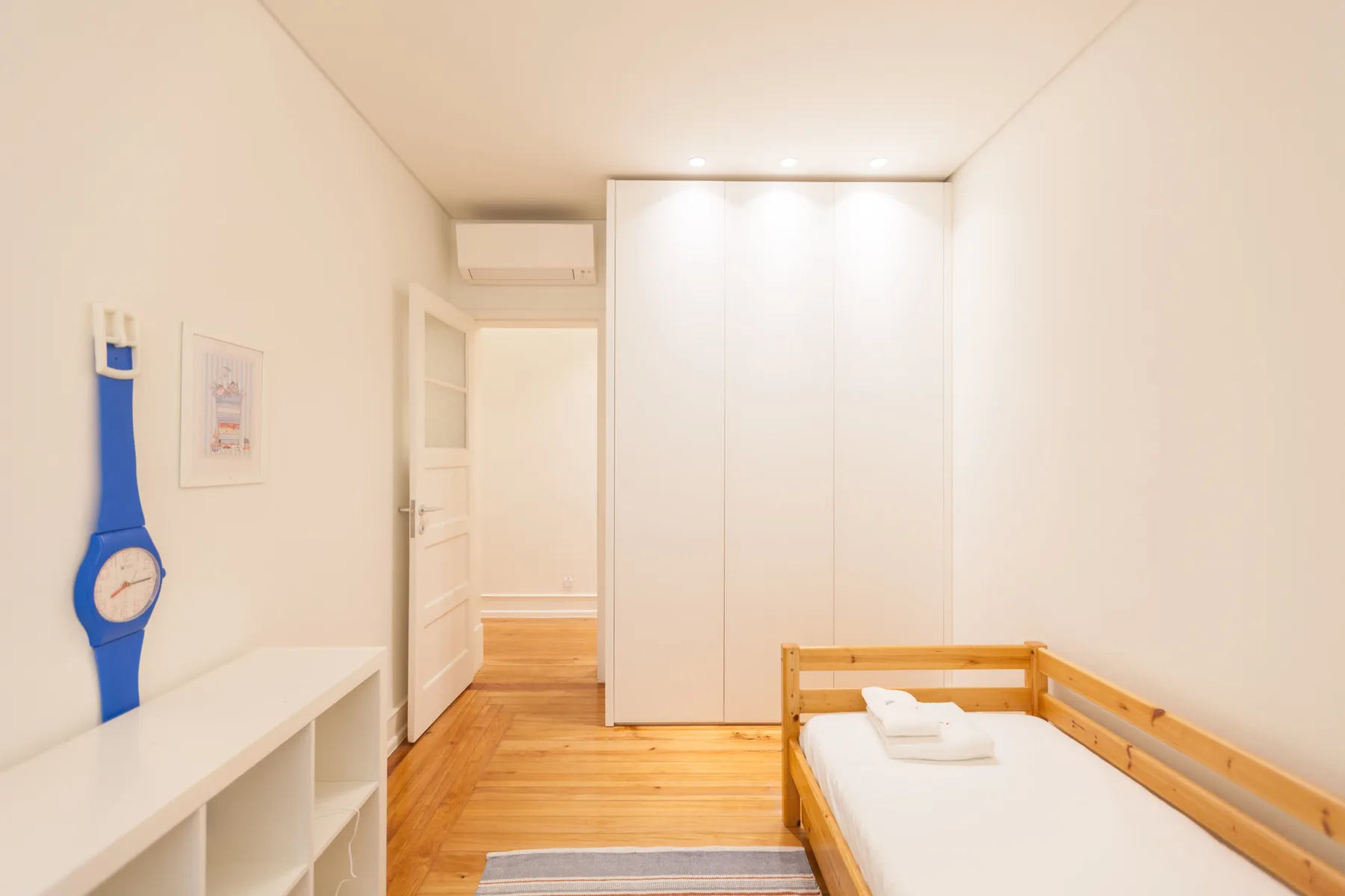 Un dormitorio luminoso con cama de madera, armario blanco y suelo de madera clara.