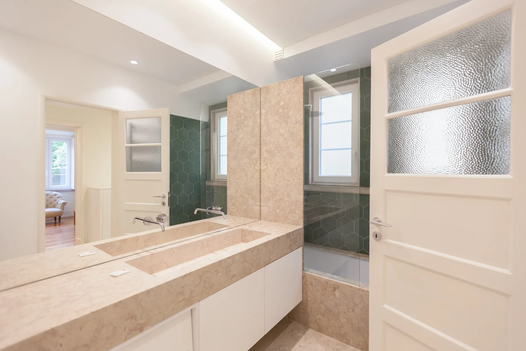Un baño luminoso con una larga encimera de lavabo y una ducha de vidrio.