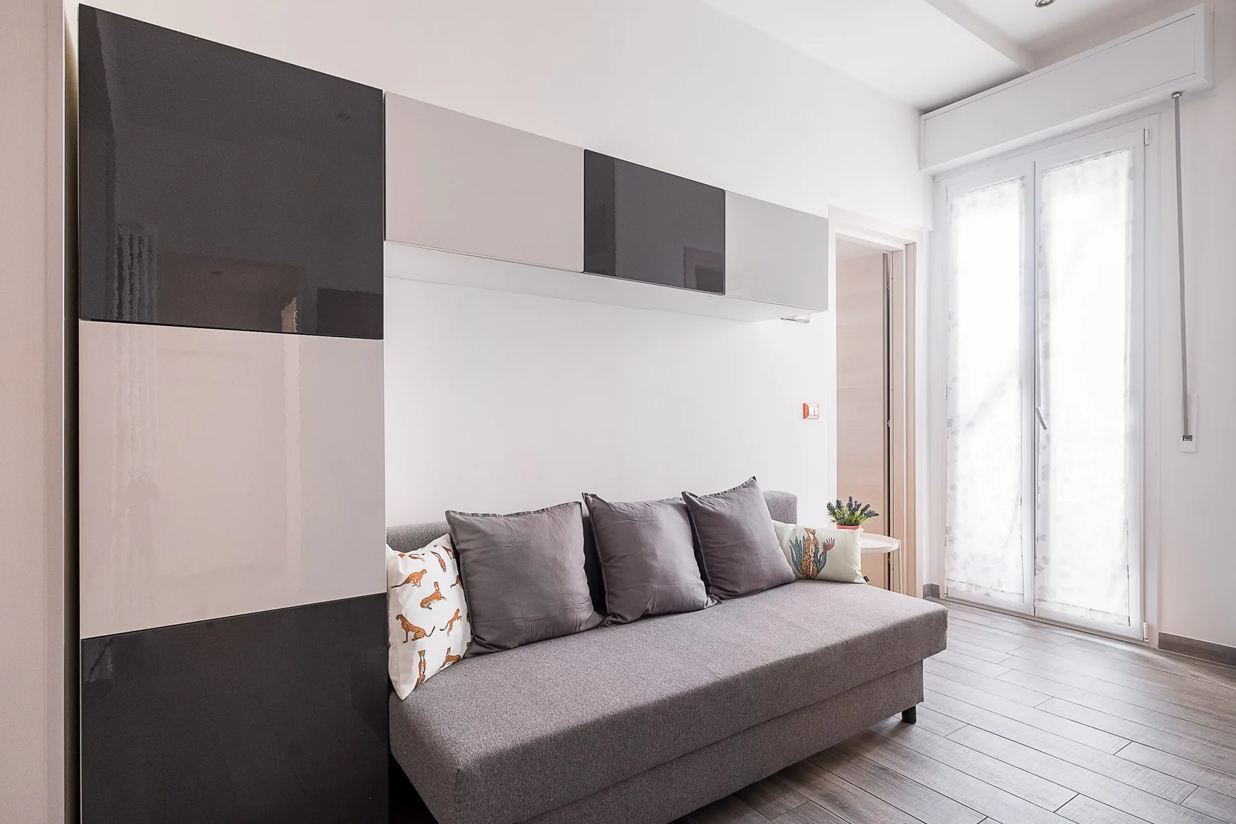 A bright living room with a gray sofa beneath wall-mounted cabinets.
