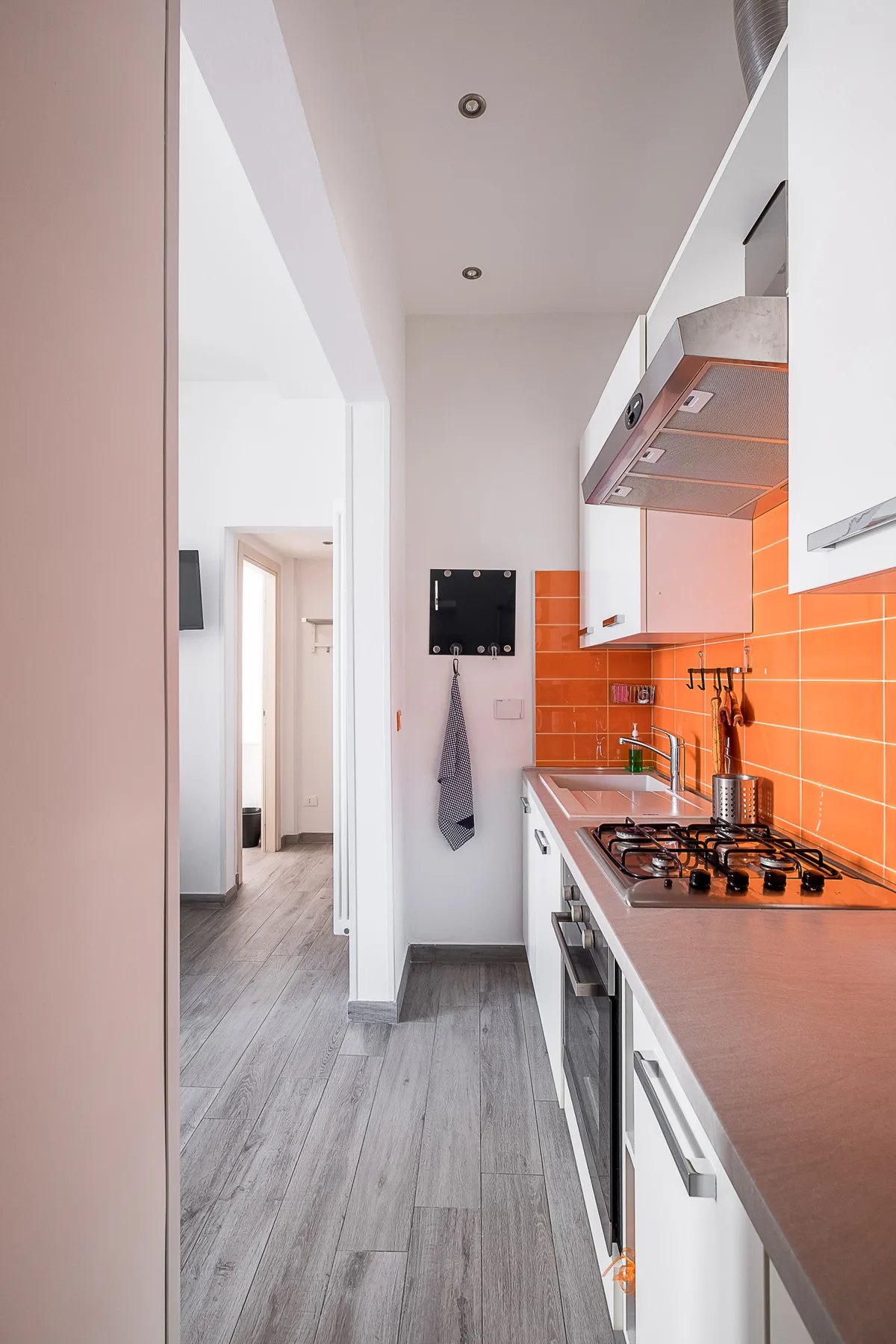 A narrow kitchen with white cabinets, an orange tile backsplash, and gray flooring.