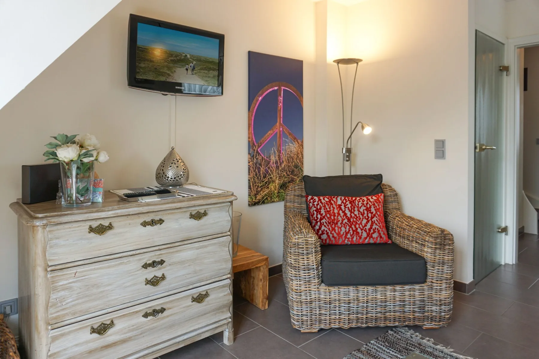 A cozy sitting area with a wicker armchair beside a distressed wooden dresser.