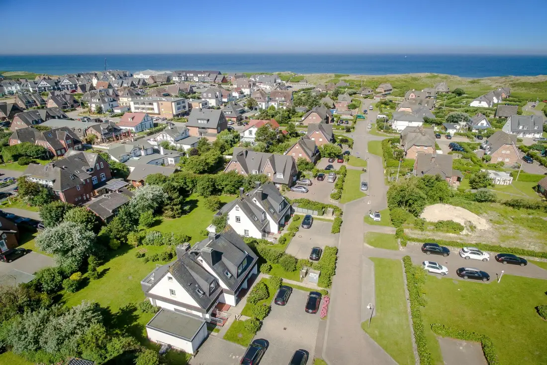 Aerial view of a coastal residential neighborhood with houses and the sea beyond.