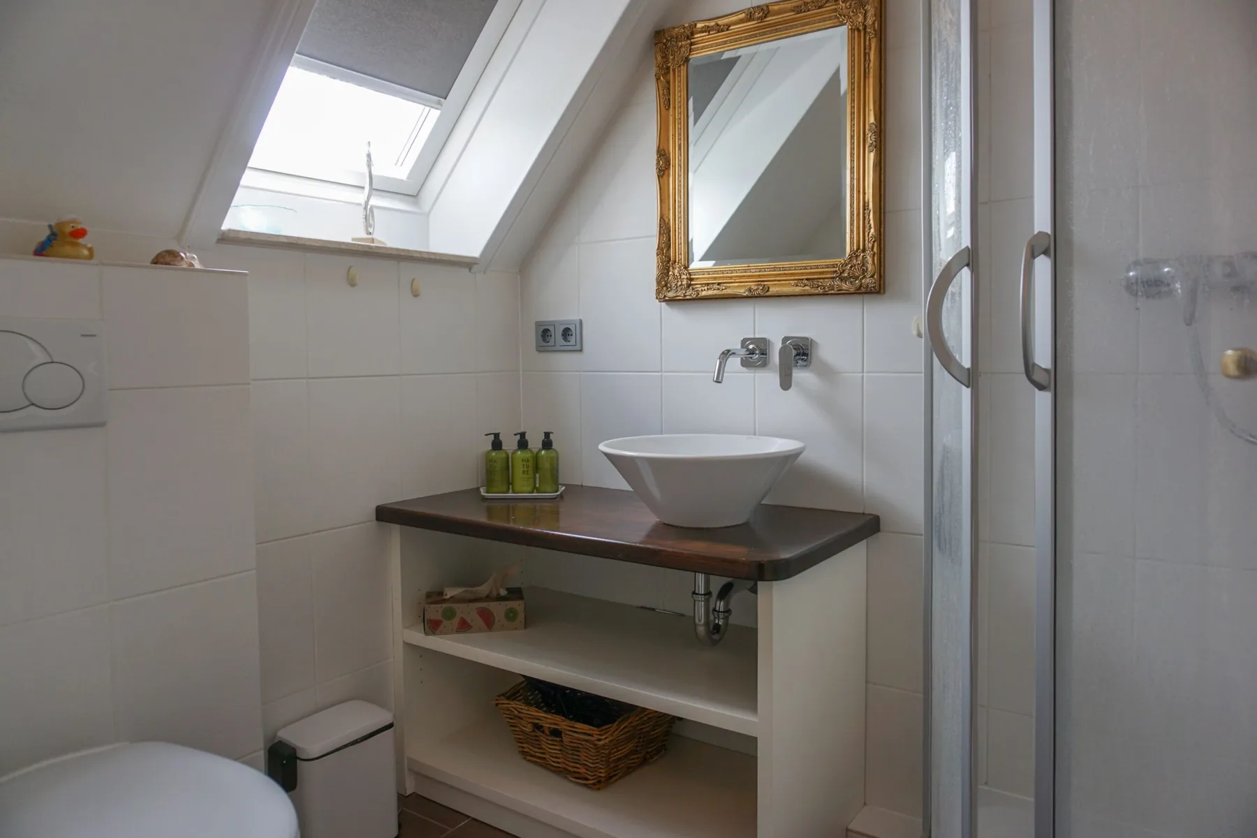 A bathroom with a vessel sink beneath a gold-framed mirror and a skylight.