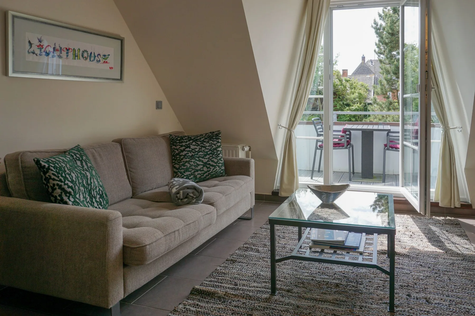 A living room with seating and a glass coffee table beside large windows.