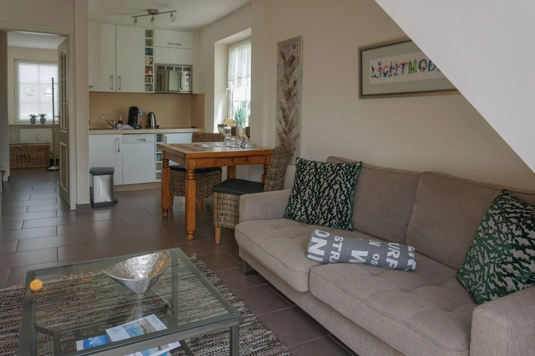 A living room with a sofa and glass coffee table, adjoining an open kitchen and dining area.