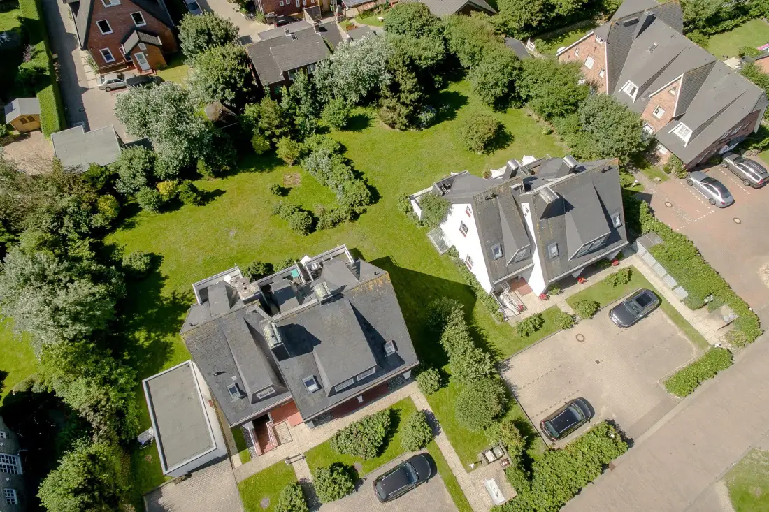 An aerial view of residential homes surrounded by lawns, trees, and paved parking areas.