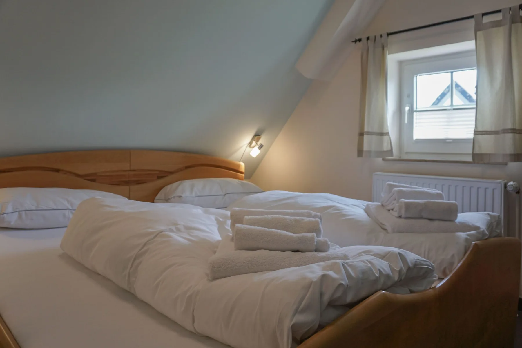 A bedroom with beds dressed in white linens and a window with curtains.