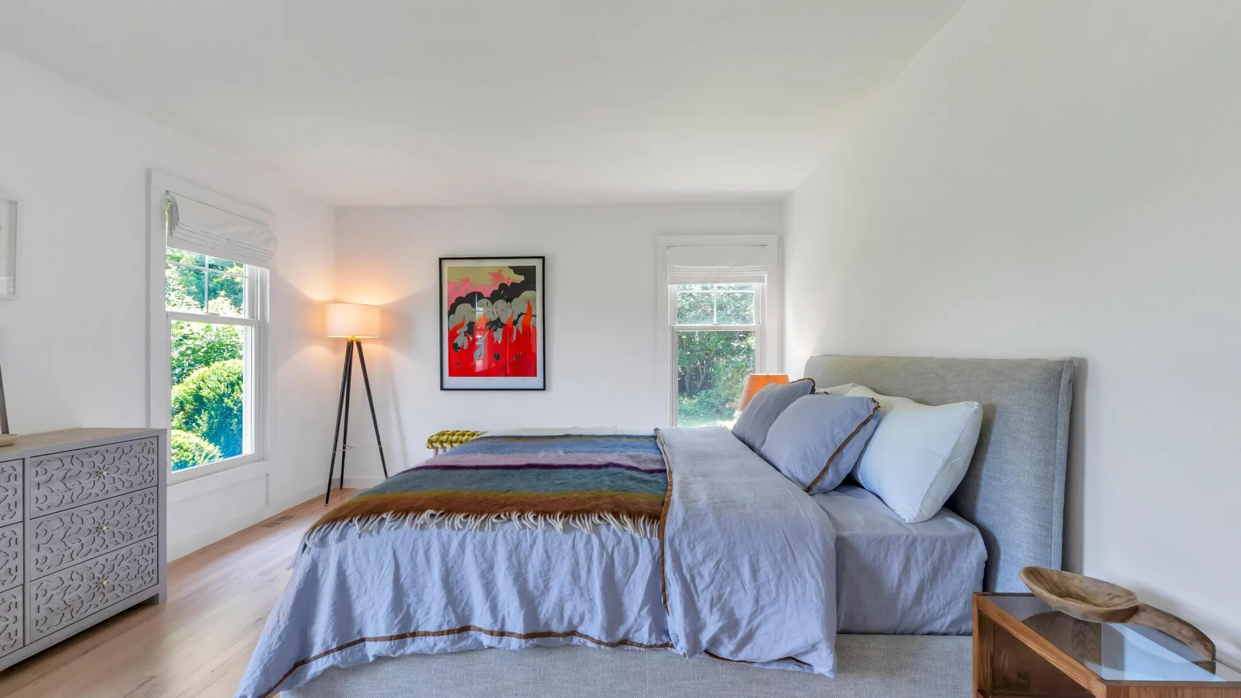 Un dormitorio luminoso con una cama, una lámpara y ventanas.