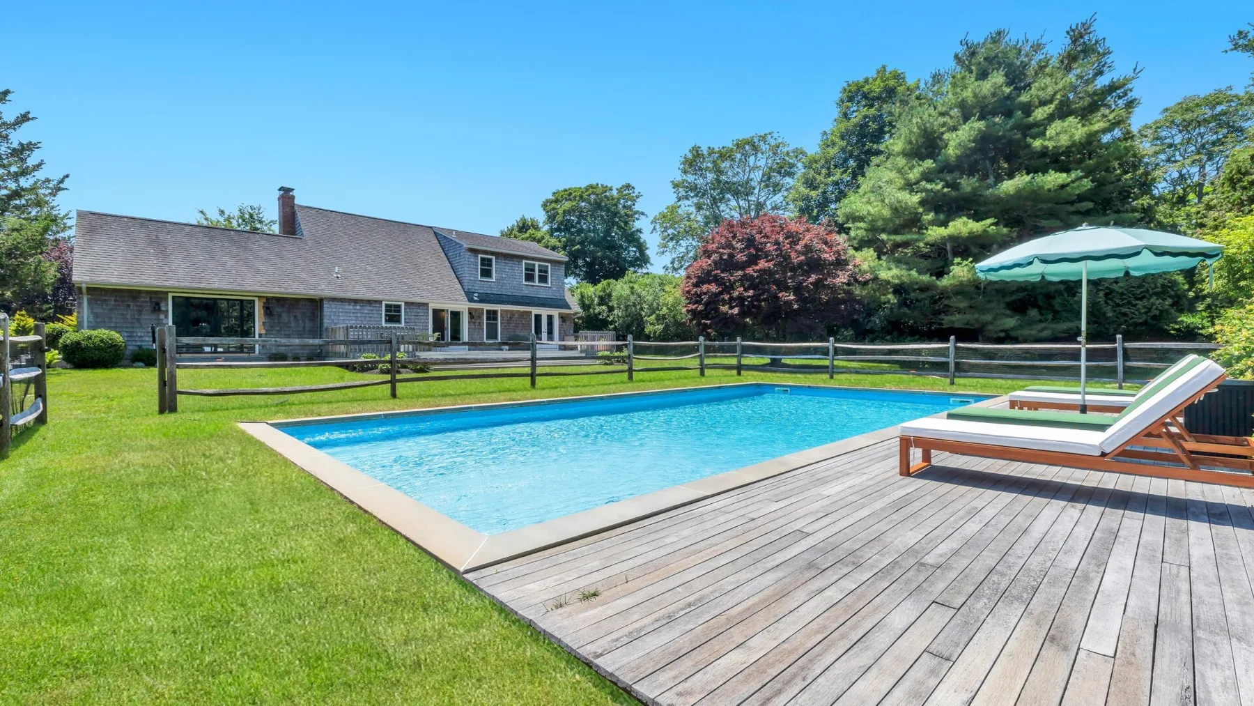Una piscina al aire libre junto a una terraza de madera y una casa.