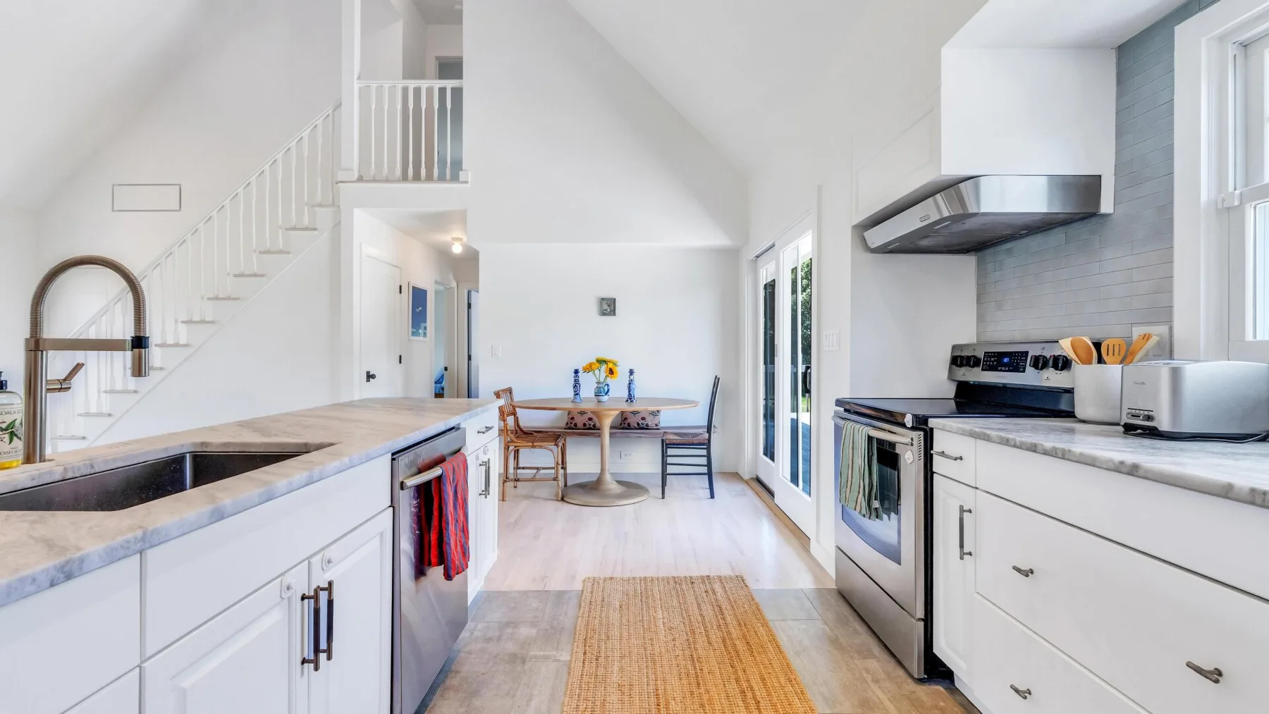 Una cocina abierta y luminosa con comedor y una escalera al fondo.