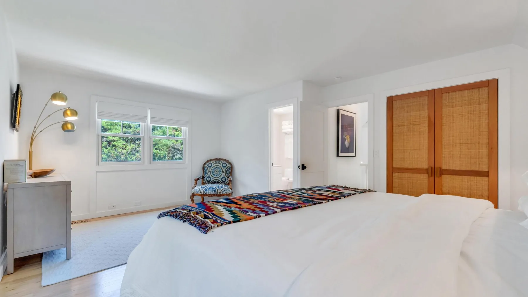Un dormitorio luminoso con una cama grande, una ventana y puertas de armario de madera.