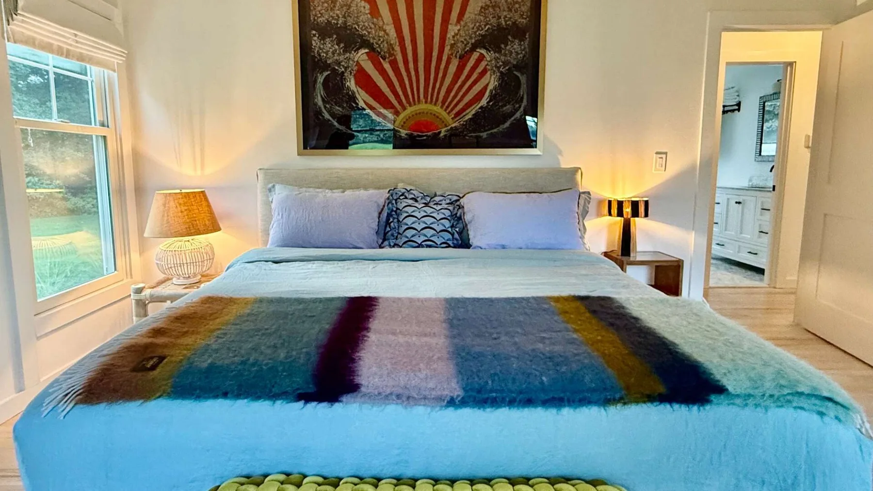 Un dormitorio con una cama bien tendida y una obra colorida sobre el cabecero.