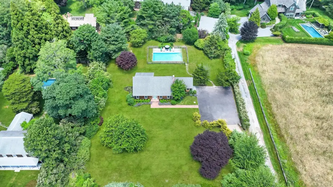Vista aérea de una propiedad ajardinada con una casa, césped y piscina.