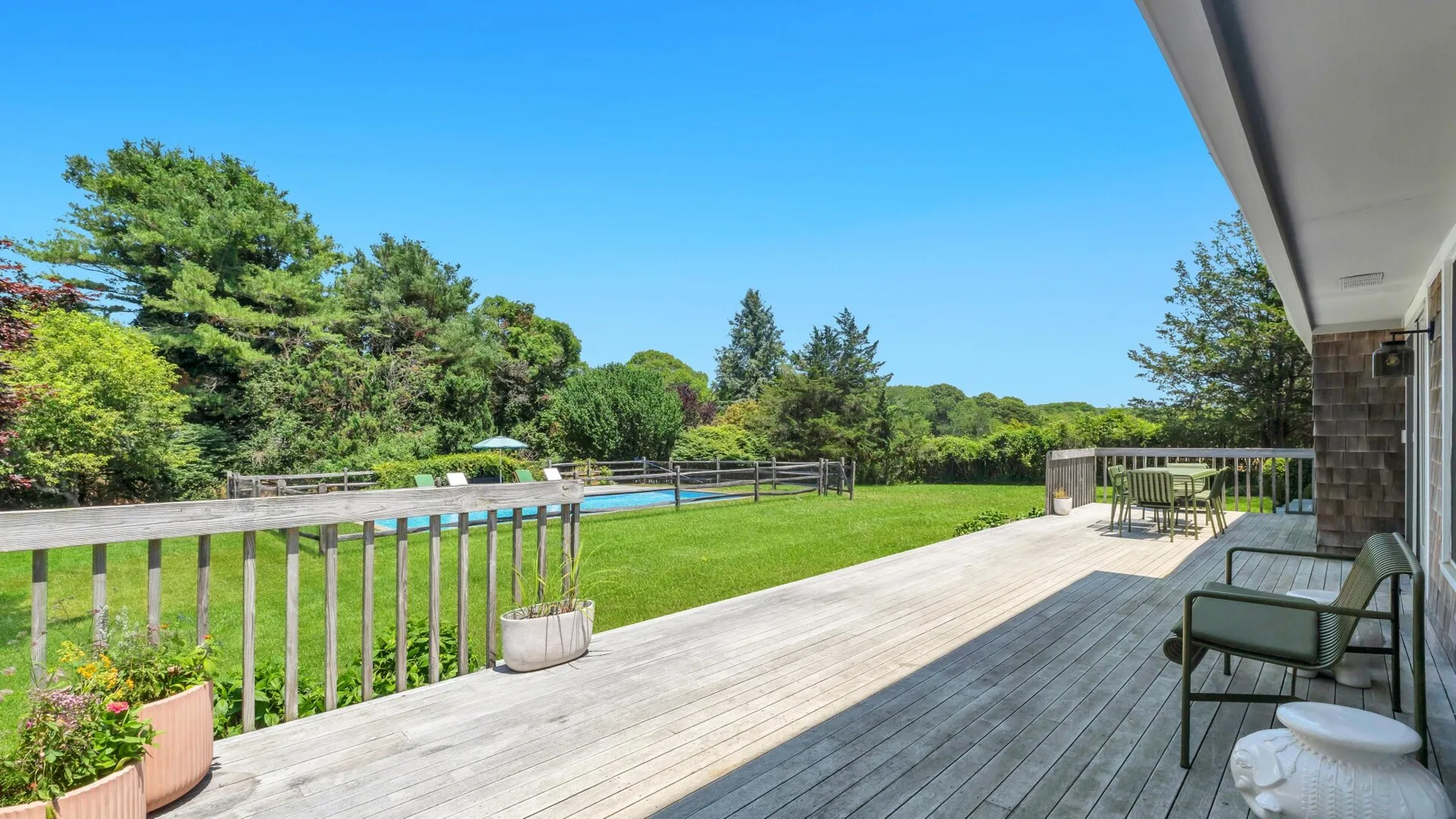 Una terraza exterior soleada da a un césped verde, un jardín y una piscina.