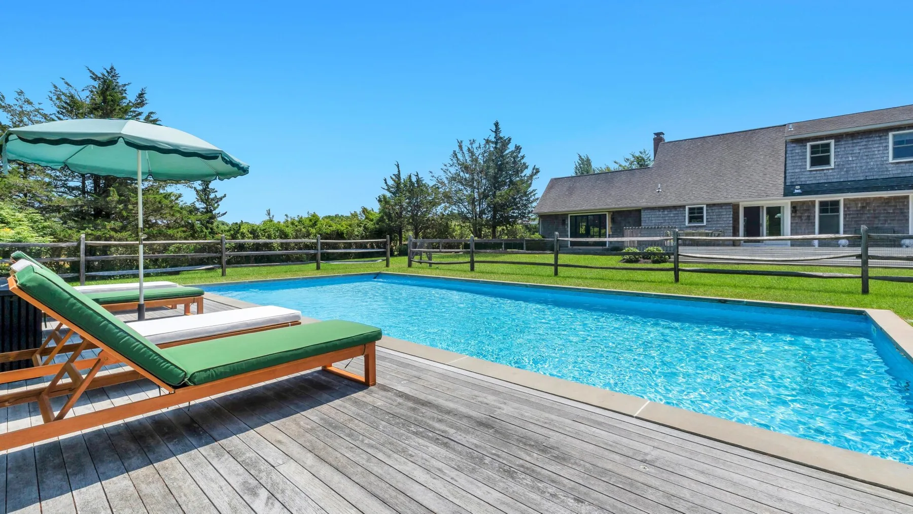 Piscina al aire libre junto a una terraza de madera con asientos.