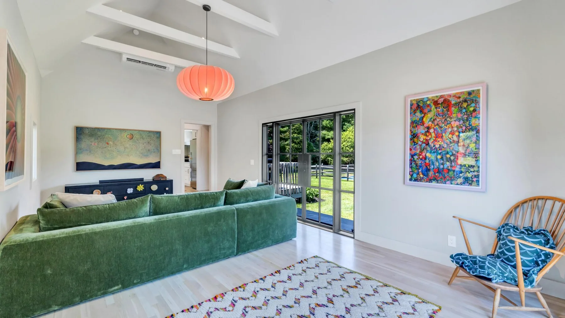 Una sala luminosa con asientos verdes, puertas de vidrio y arte colorido en la pared.