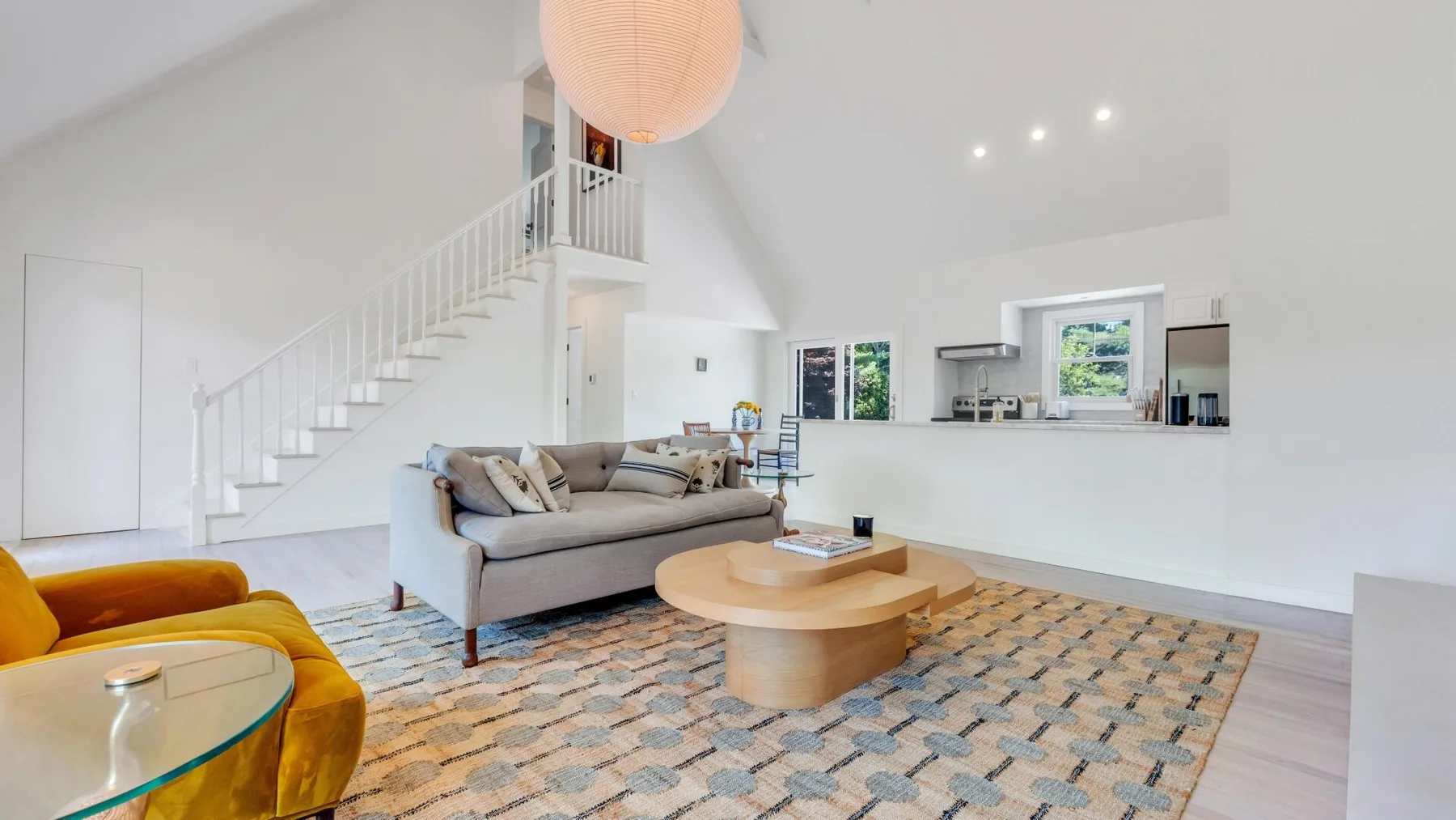 Una sala luminosa con una escalera, asientos y una mesa de centro redonda.